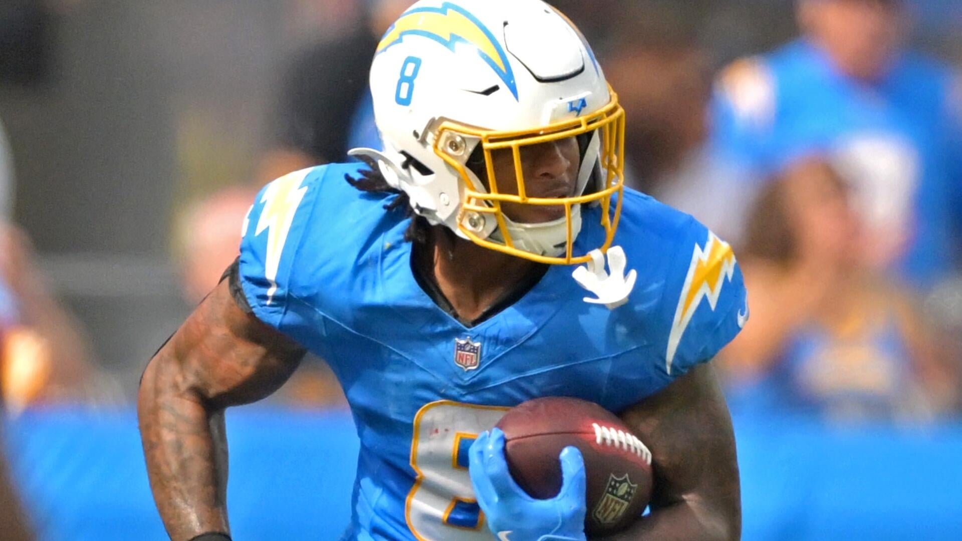A football player wearing a blue jersey with the number 8 and a white helmet with a lightning bolt logo runs forward while carrying a football.