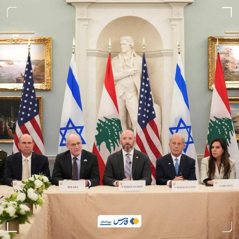 Five officials sit at a table labeled "Israel," "United States," and "Lebanon," flanked by U.S., Israeli, and Lebanese flags, with a George Washington statue visible behind them.