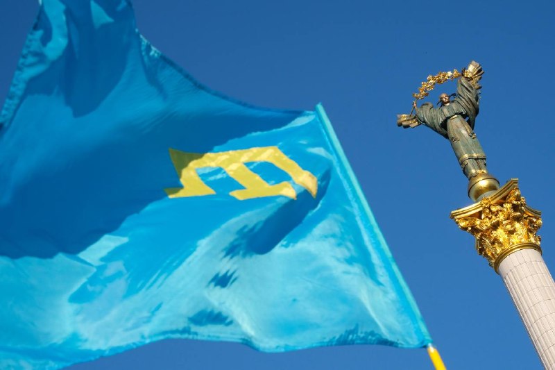 A heavily damaged overpass bridge with broken concrete spans and exposed rebar sits above a debris-strewn roadway, marked with Ukrainian military text and a trident emblem.