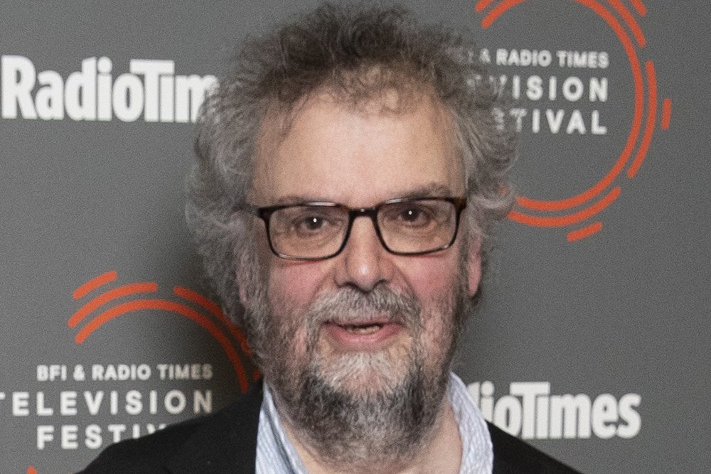 A man with gray curly hair, a beard, and glasses stands before a backdrop displaying "Radio Times" and "BFI & Radio Times Television Festival" logos.