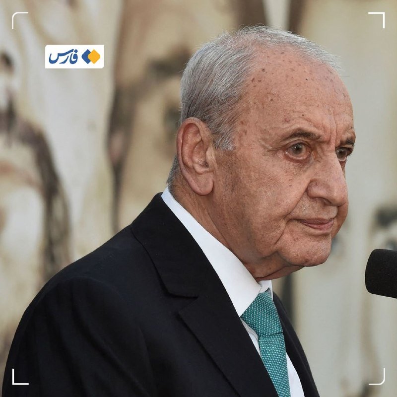 An elderly man with gray hair, wearing a black suit and green tie, speaks near a microphone with a Persian news logo overlay.