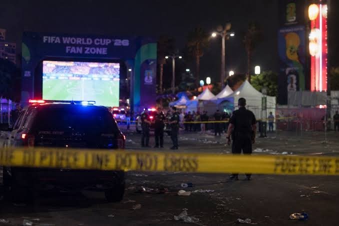 Police and emergency vehicles are stationed outside a "FIFA World Cup '26 Fan Zone" at night, behind yellow police tape cordoning off a debris-strewn area.
