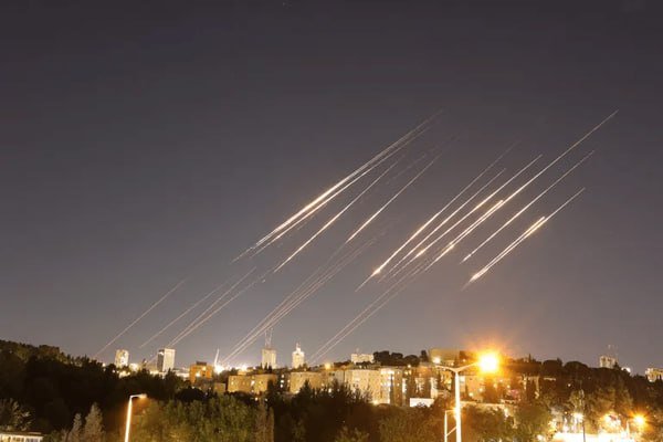 Multiple bright streaks of light trail across the night sky above an illuminated city skyline.