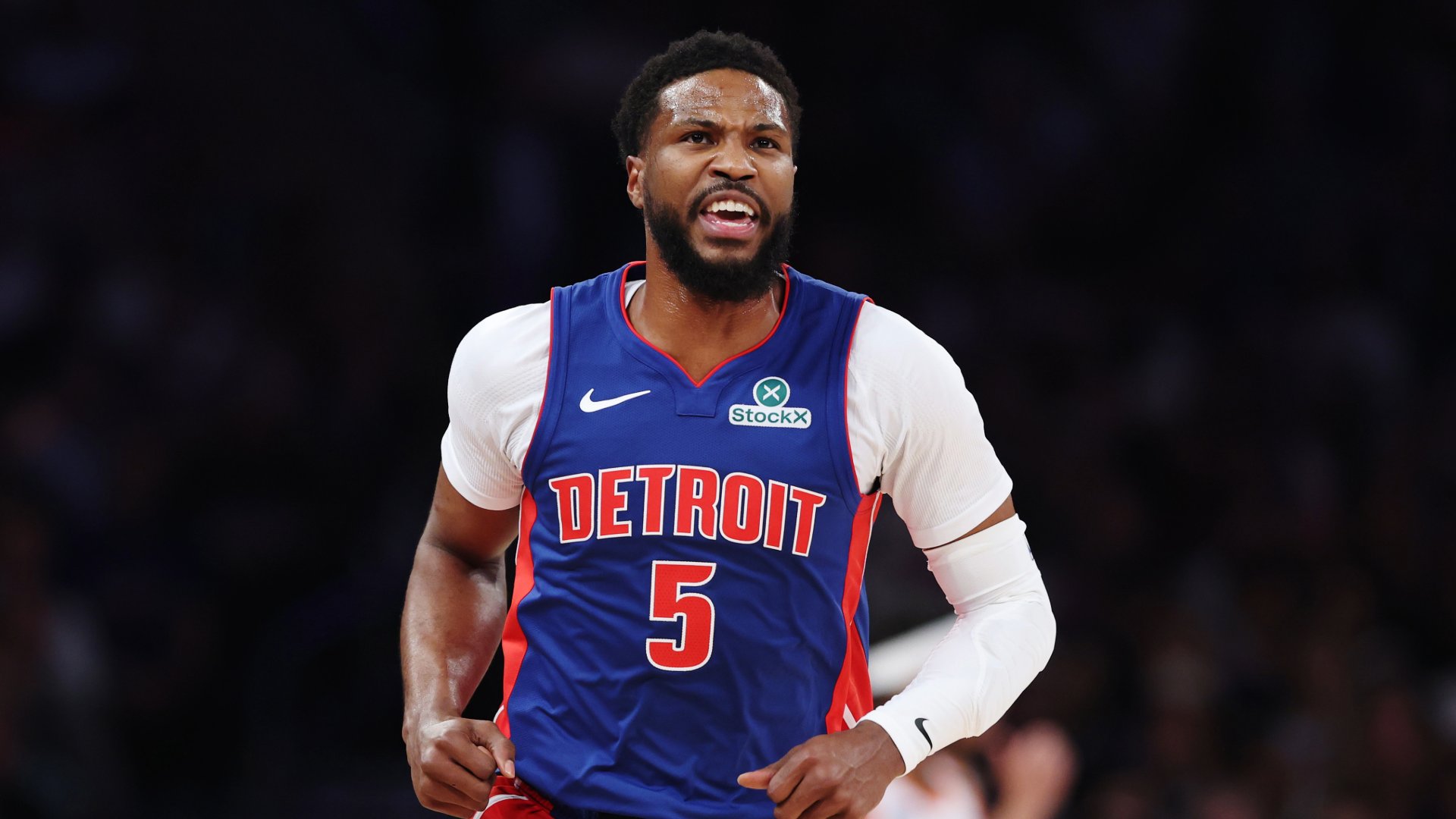 A Detroit basketball player wearing jersey number 5 reacts with an open-mouthed expression during a game in a darkened arena.