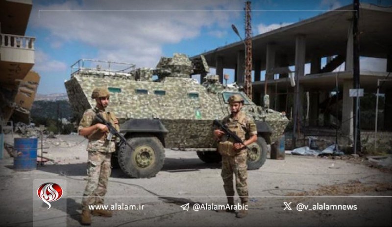 Two armed soldiers in camouflage uniforms stand beside an armored military vehicle on a debris-strewn street near damaged buildings.