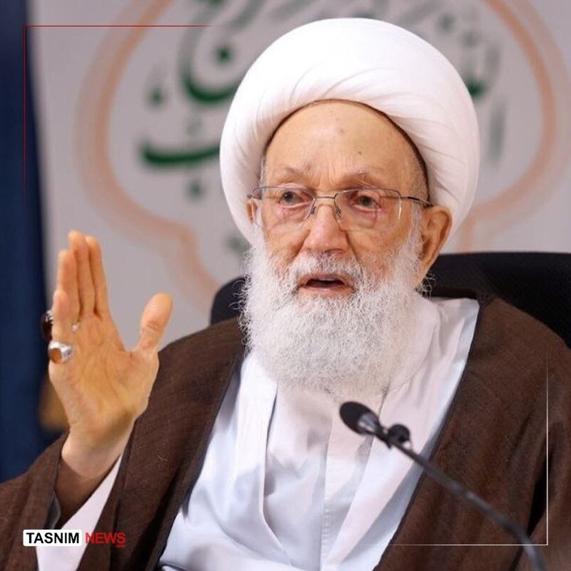 An elderly bearded cleric in a white turban and clerical robes speaks into a microphone, gesturing with his raised right hand, with a "Tasnim News" watermark visible.