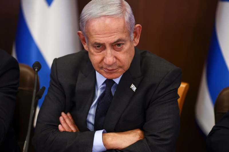 A man in a dark suit speaks at a UN-style conference table with a placard reading "IRAN (ISLAMIC REPUBLIC OF)," with a UN emblem visible in the background.
