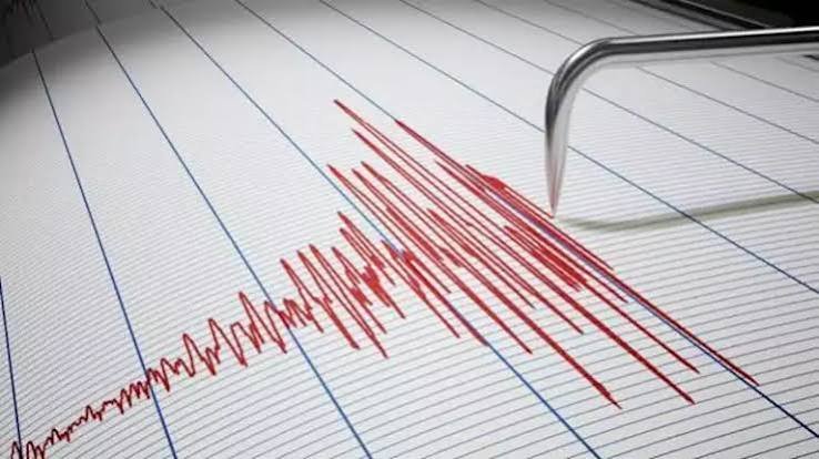 A seismograph needle traces a jagged red line of earthquake activity across lined graph paper, spiking sharply before tapering off.