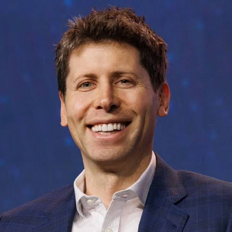 A smiling man with short brown hair wearing a dark blazer and light button-up shirt poses in front of a blue backdrop.