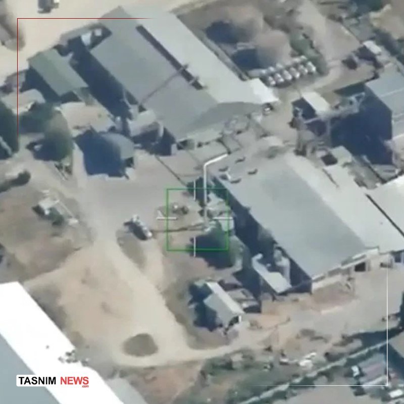 Aerial surveillance footage shows an industrial facility with large buildings, storage tanks, and a targeting reticle overlay, watermarked "TASNIM NEWS."