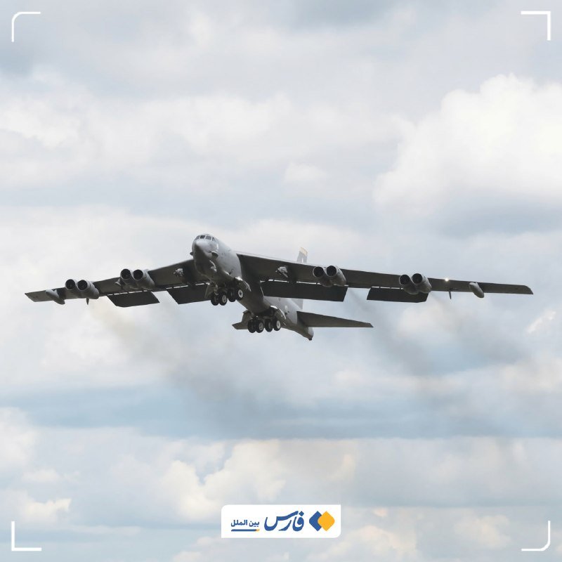 A large gray military bomber aircraft with eight engines flies through a partly cloudy sky, viewed from below.
