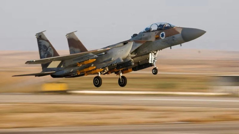 A twin-tail fighter jet with desert camouflage takes off from a runway, landing gear extended.
