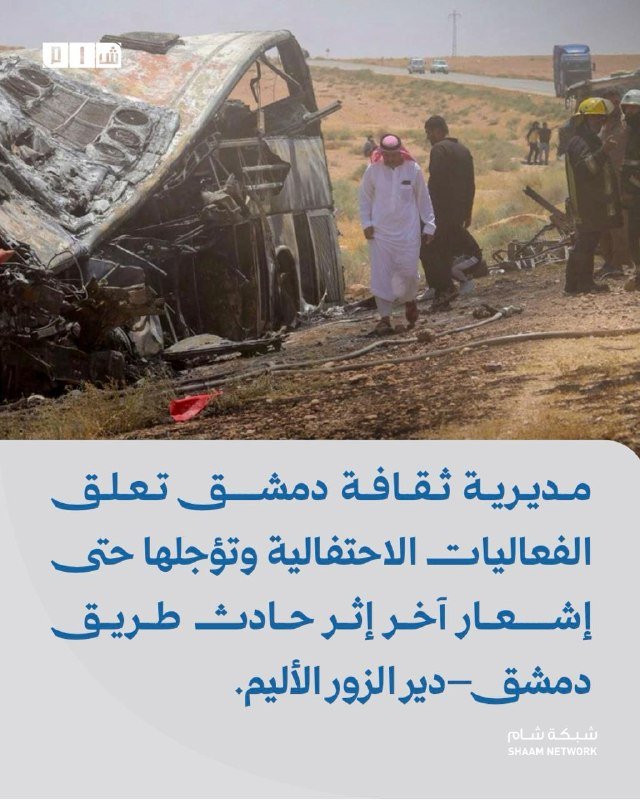 A burned, overturned bus lies in a roadside field as men in traditional dress and rescue workers inspect the wreckage.