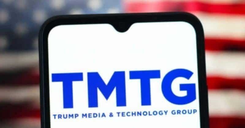 A smartphone displays the "TMTG - Trump Media & Technology Group" logo against a blurred American flag background.