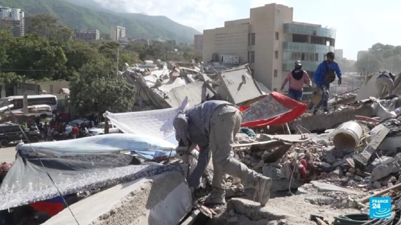 Rescue workers search through massive concrete rubble amid damaged high-rise buildings in a hazy urban area.