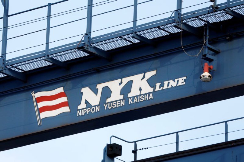 A blue industrial crane displays the "NYK Line Nippon Yusen Kaisha" logo alongside a striped flag graphic.