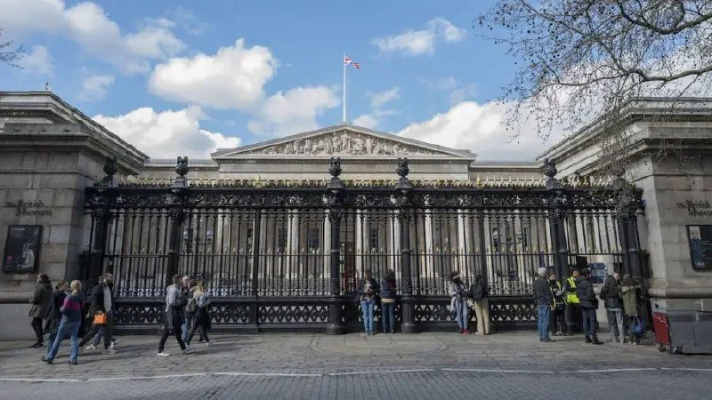Visitors gather outside the ornate iron gates and neoclassical stone facade of a museum building beneath a partly cloudy sky.