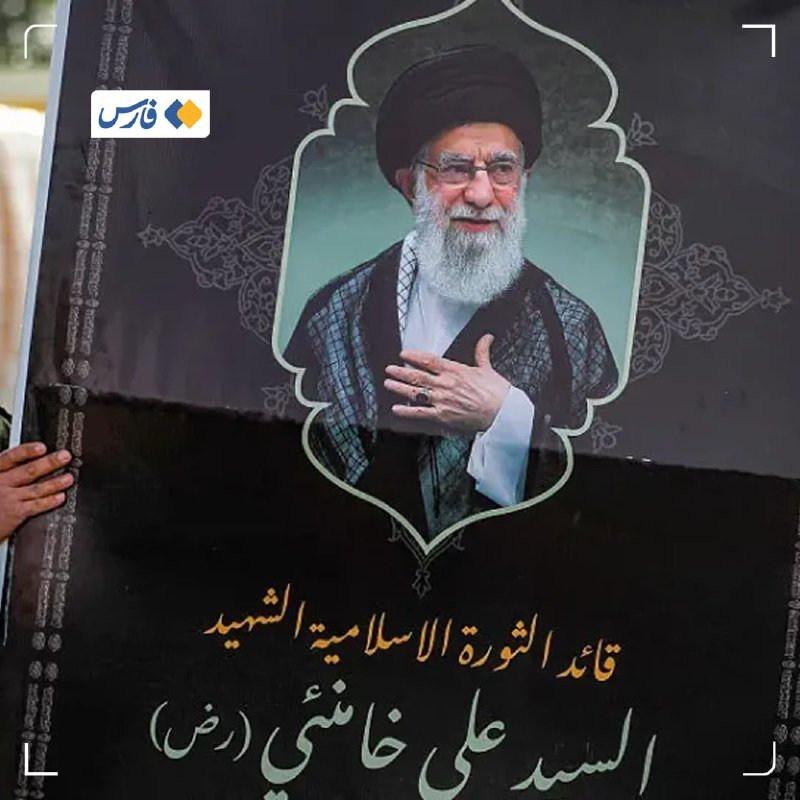 A printed graphic displays a framed portrait of a bearded cleric in clerical attire above Arabic script on a dark background, held by a visible hand.