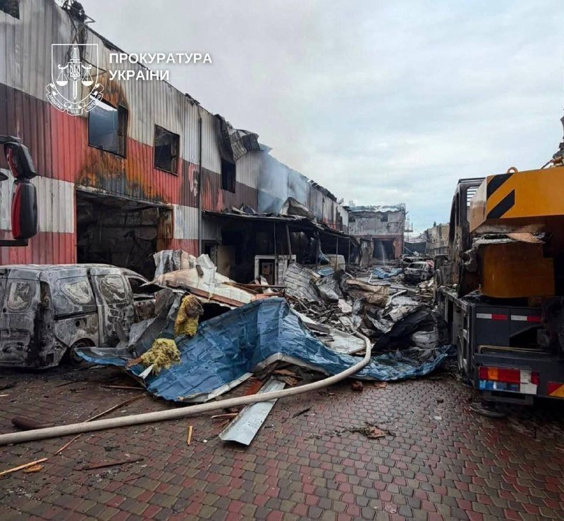 A watermark reading "ПРОКУРАТУРА УКРАЇНИ" appears over a scene of a burned, partially collapsed commercial building with charred vehicles and scattered debris on a brick-paved area.