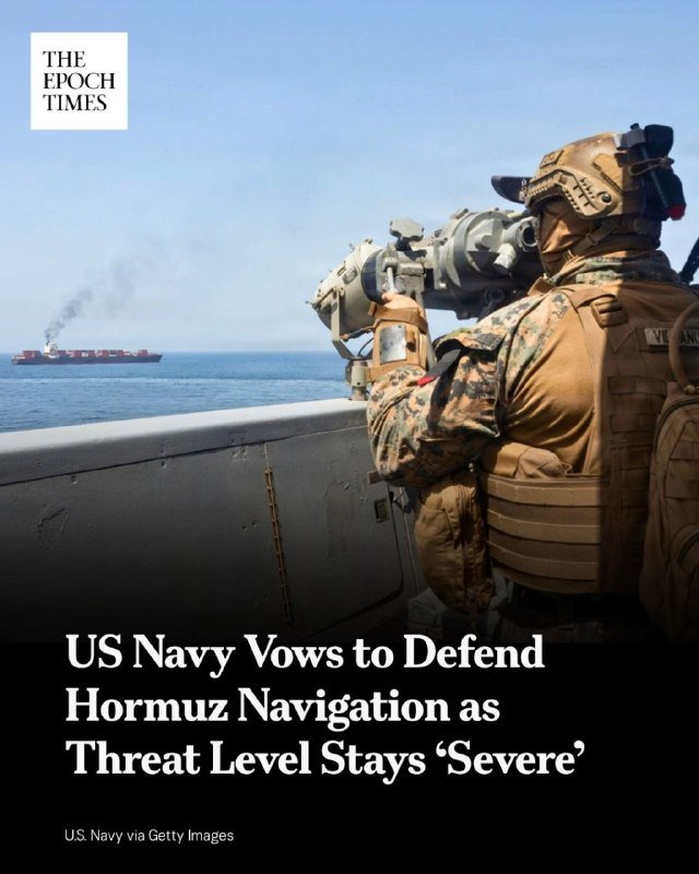 A Navy servicemember in camouflage and tactical gear aims a shoulder-mounted weapon from a ship's railing toward a distant smoke-emitting cargo vessel on the open sea.