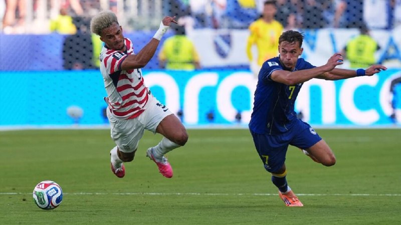 A soccer player wearing a dark USA jersey with the number 20 controls a soccer ball mid-air in a crowded stadium.