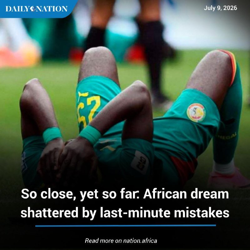 A football player in a green Senegal kit lies on the pitch, covering his face with his hands in apparent despair.