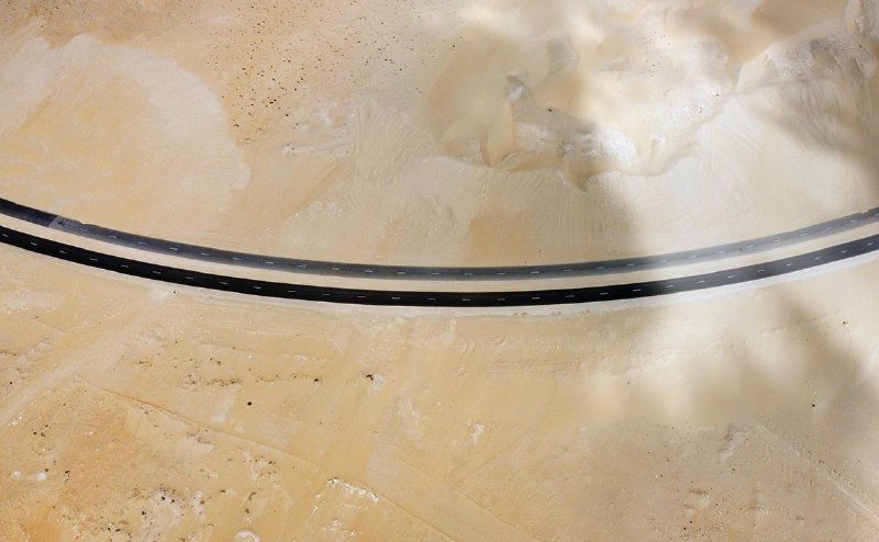 An aerial view shows a curving two-lane asphalt road traversing a barren, sandy desert landscape.
