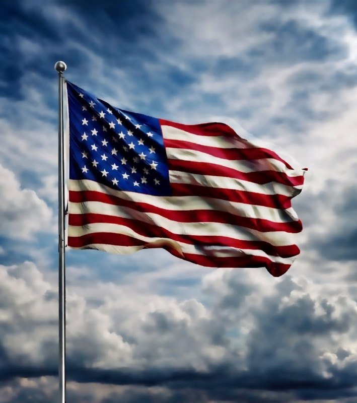 An American flag waves in the wind atop a silver pole against a backdrop of partly cloudy skies.
