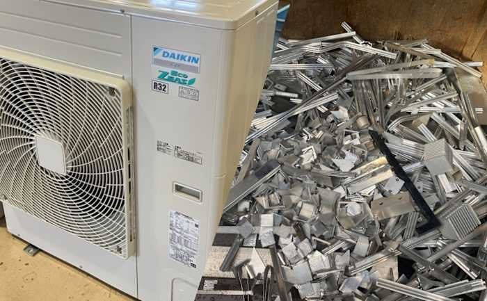 A Daikin air conditioning unit sits beside a large pile of scattered aluminum scrap pieces.