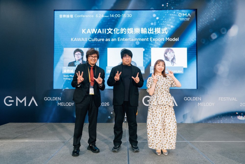 Three people pose with peace signs on stage at the Golden Melody Festival 2026 conference titled "KAWAII Culture as an Entertainment Export Model."