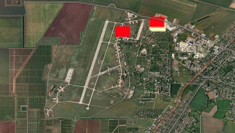 A satellite image shows an airfield with runways, hangars, and parked aircraft next to a town, with two opaque red rectangles obscuring portions of the base.