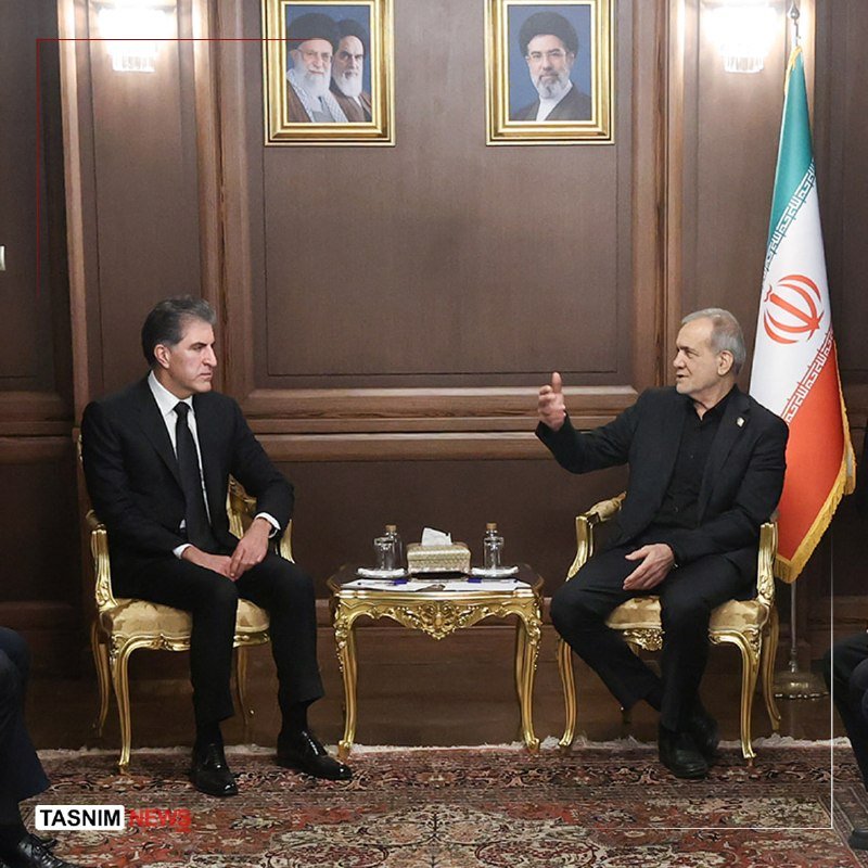 Two delegations in business attire sit facing each other across a long conference table, with two small flags placed at the center.