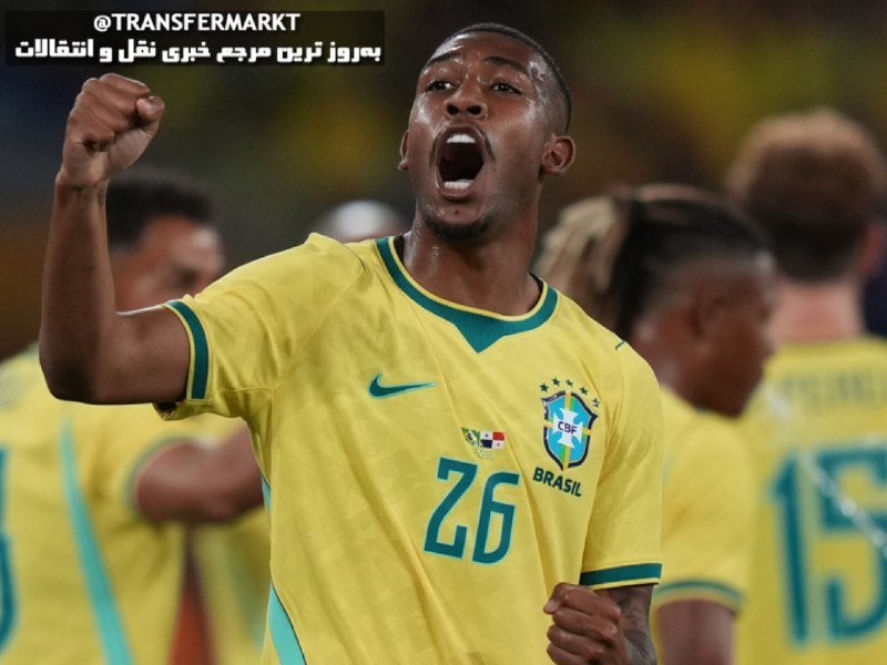 A soccer player wearing a yellow Brazil jersey with the number 26 celebrates with a raised fist and open mouth, with teammates visible in the background.