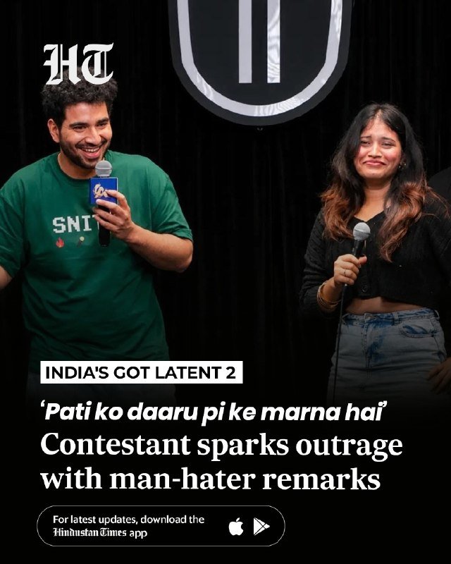 A man in a green t-shirt holding a microphone smiles beside a woman also holding a microphone, in front of a black backdrop with a shield logo.