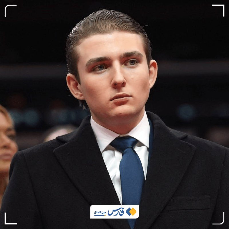 A young man in a black coat, white shirt, and blue tie looks forward with a serious expression at a crowded event, with an Arabic/Persian logo visible below.