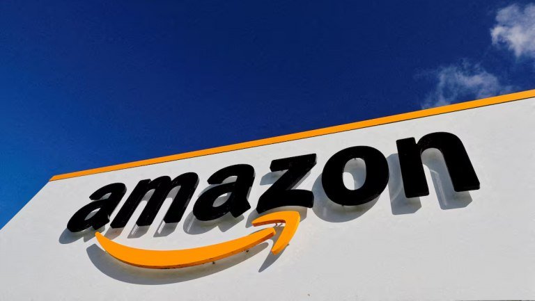 A large white sign with an orange border displays the Amazon logo against a blue sky with scattered clouds.