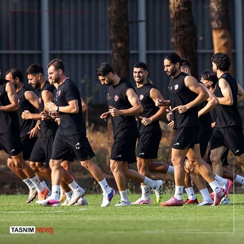 A group of men in matching black athletic shirts and shorts jog together across a grass field during a training session.