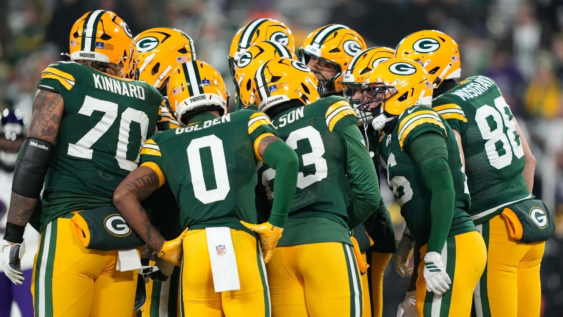 Green Bay Packers players in green and yellow uniforms huddle together on the field, with names including Kinnard, Golden, and Musgrave visible on their jerseys.