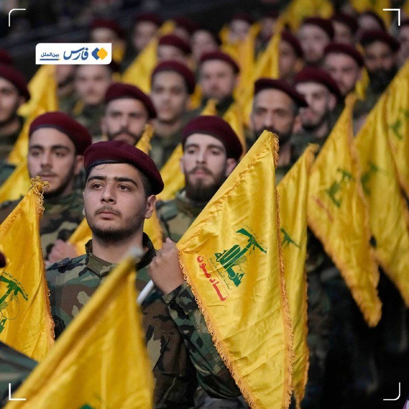 Rows of men in camouflage uniforms and maroon berets hold yellow flags featuring green and red insignia, standing in formation.