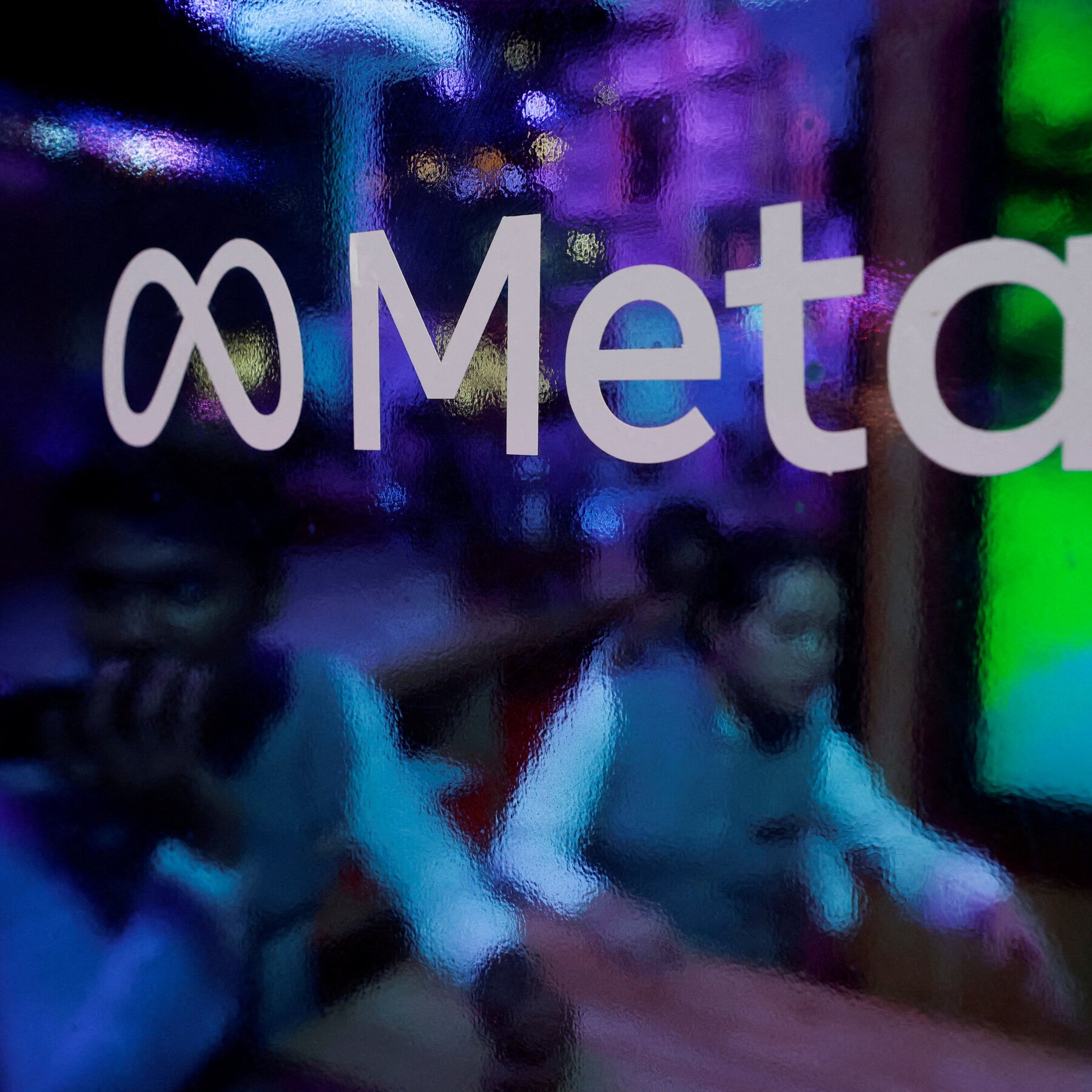 Close-up of the Meta logo on a textured glass surface illuminated by purple, blue, and green lighting.