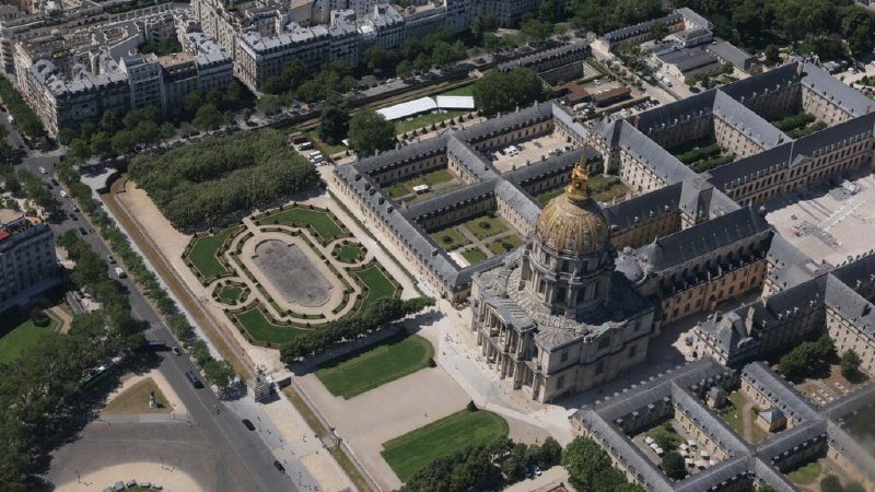 An aerial photograph captures the golden-domed Les Invalides complex in Paris, featuring formal gardens, tree-lined pathways, and surrounding urban architecture.