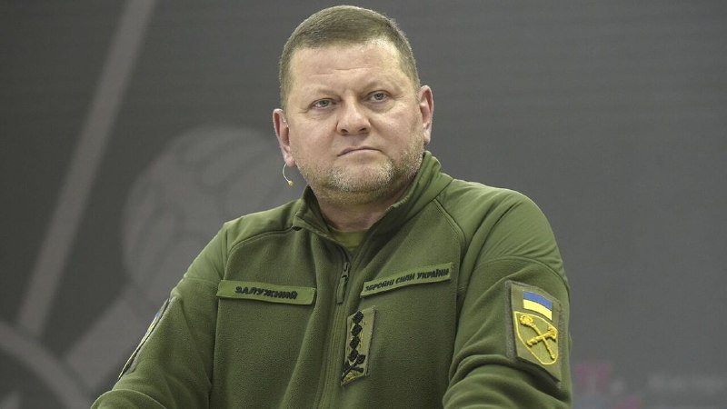 A man in an olive green military fleece with Ukrainian insignia and name tapes sits at what appears to be a press briefing.