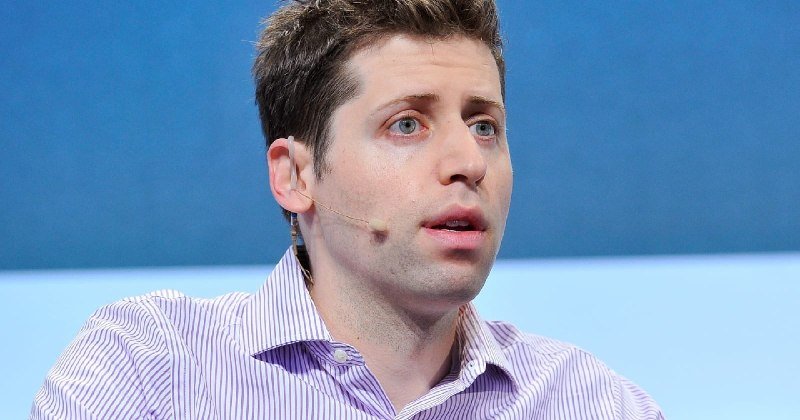 A man with short brown hair wearing a striped collared shirt and an earpiece speaks against a blue background.