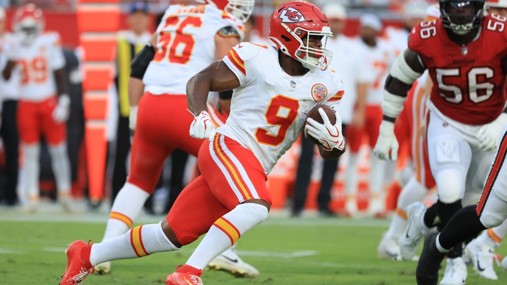 A Kansas City Chiefs player wearing number 9 carries the football while running during an NFL game against a team in red jerseys.