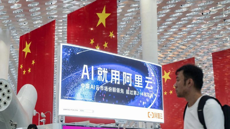 A man stands beside a digital billboard displaying Chinese characters and a globe graphic, with large Chinese national flags hanging in the background.
