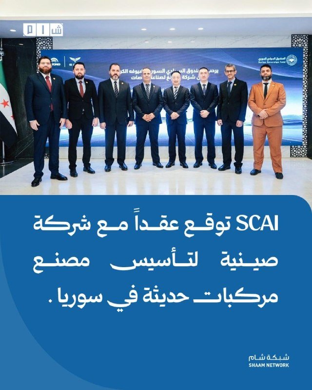 Seven men in suits pose for a photo in front of a blue backdrop with Arabic text and logos, including "SHAAM NETWORK."