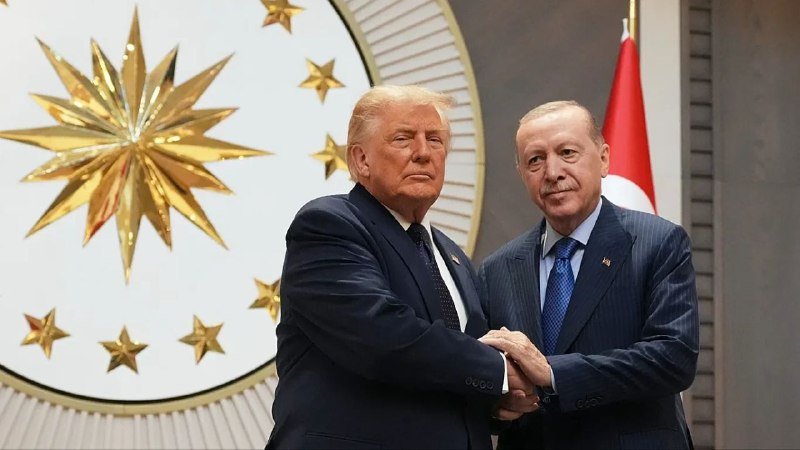 Two men in dark suits sit in black leather chairs beside a small table holding water glasses, with a backdrop displaying NATO and "Ankara" logos alongside American flags.