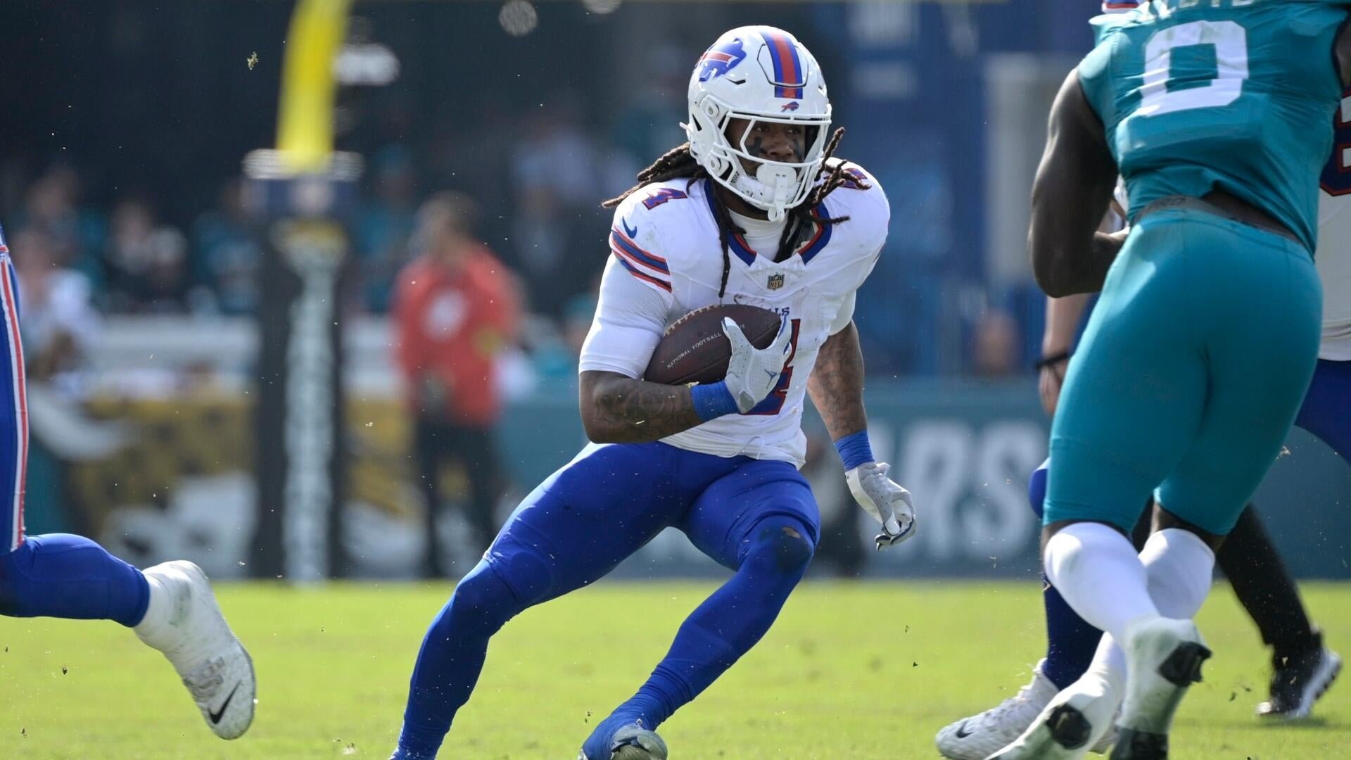 Buffalo Bills player in white uniform runs with the football while evading a teal-jerseyed defender during an NFL game.