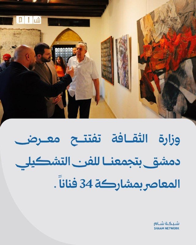 Men converse in a gallery beside large colorful abstract paintings displayed on the walls.