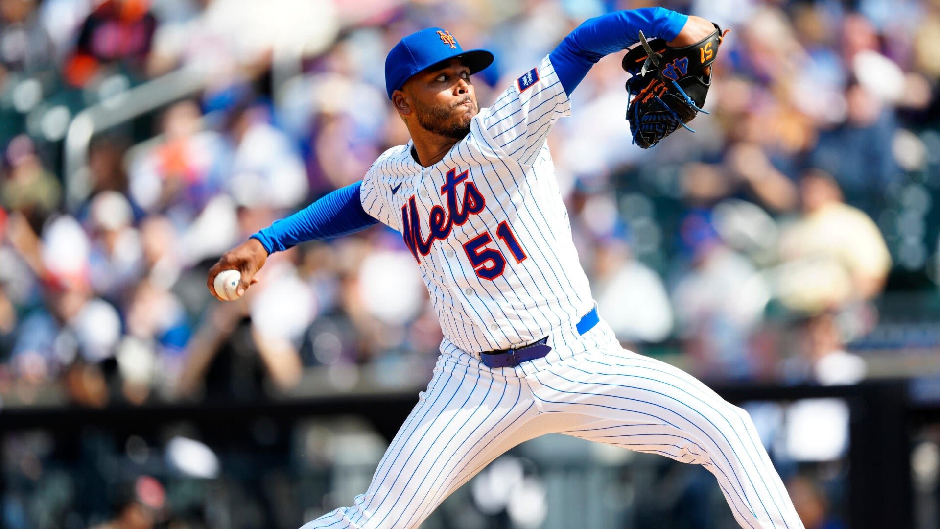 A New York Mets pitcher wearing jersey number 51 throws a pitch during a daytime baseball game in front of a crowded stadium.